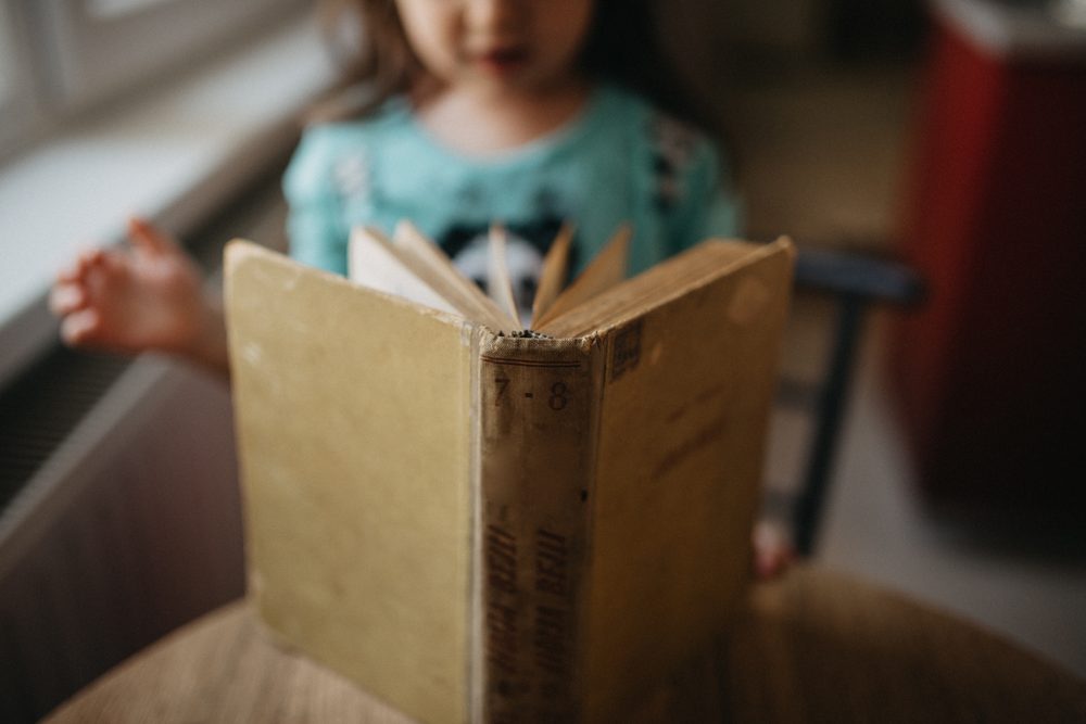 A child sitting alone at a wooden table, focused on reading