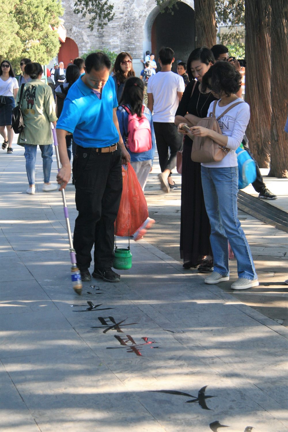A man practising water calligraphy with Chinese characters on a paved walkway in Beijing