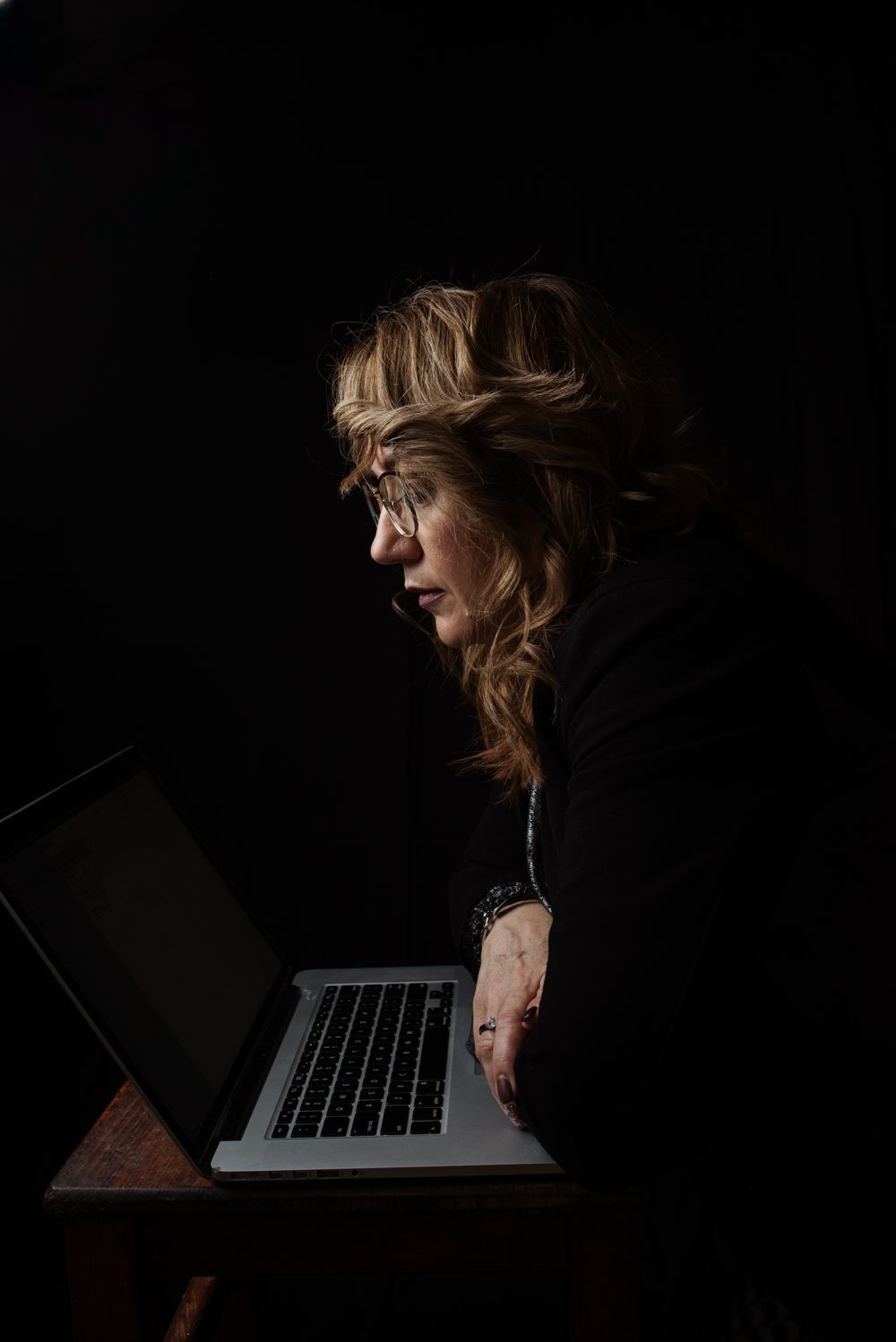Adult sitting at a desk with a laptop, deeply focused in a low-light room