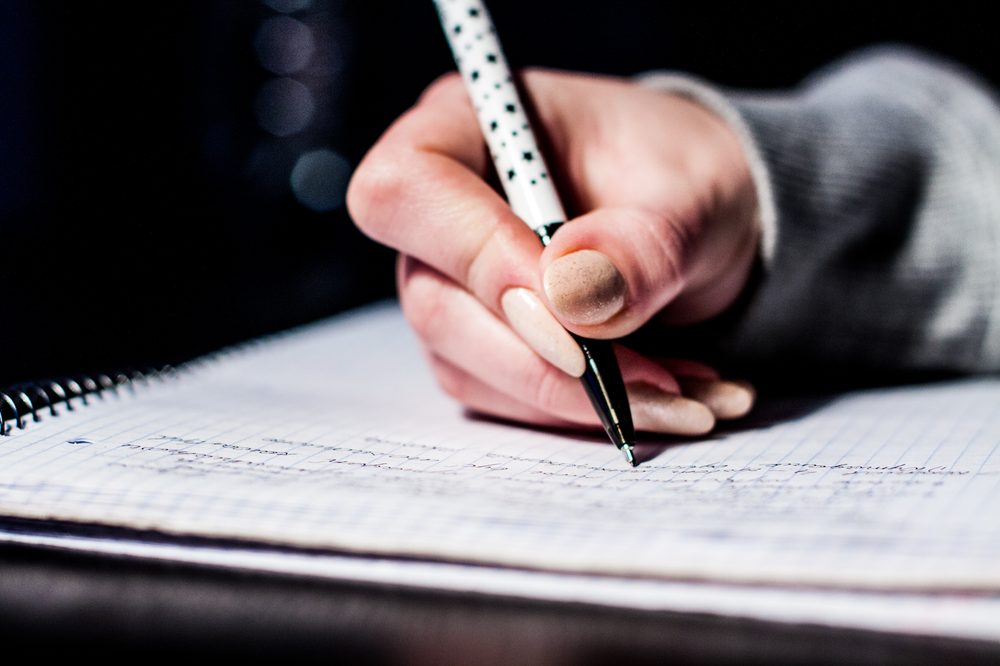 A hand writing notes with a pen, representing an alternative to flashcard drilling for vocabulary learning