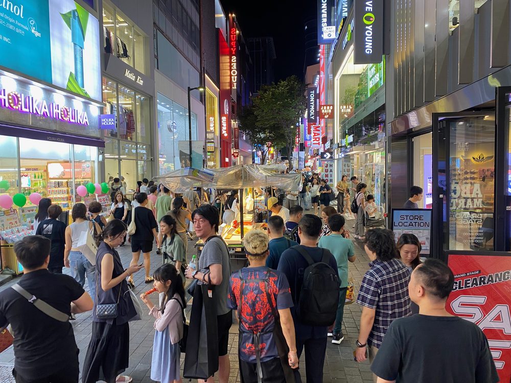 A busy night market street in Myeongdong, Seoul, with signage and stalls surrounded by everyday Korean vocabulary